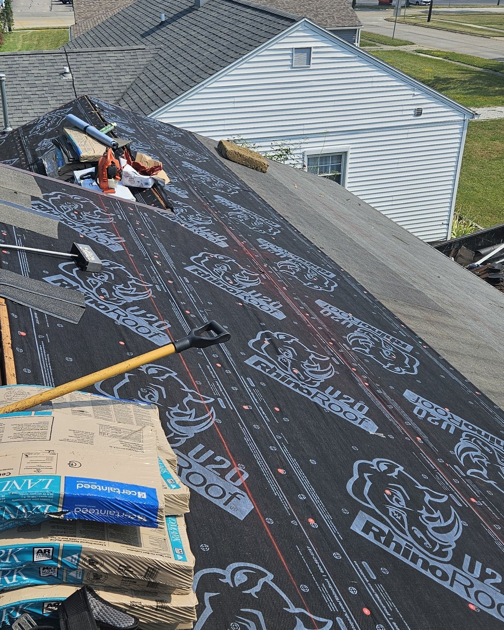 Roofing materials and tools on a sloped roof during installation, with black underlayment and gray shingles nearby