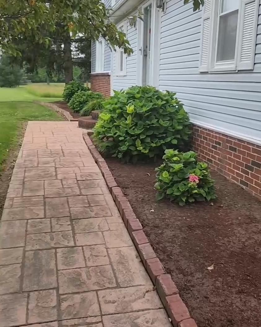 Brick walkway beside a light blue house with brick edging and green shrubs