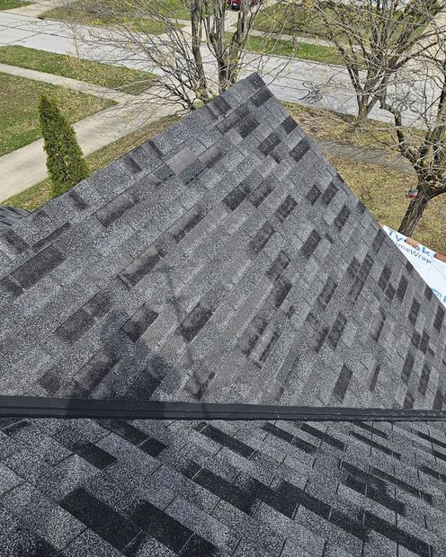 View from a shingled roof over a sidewalk and trees, with shadows across the lower roof edge.