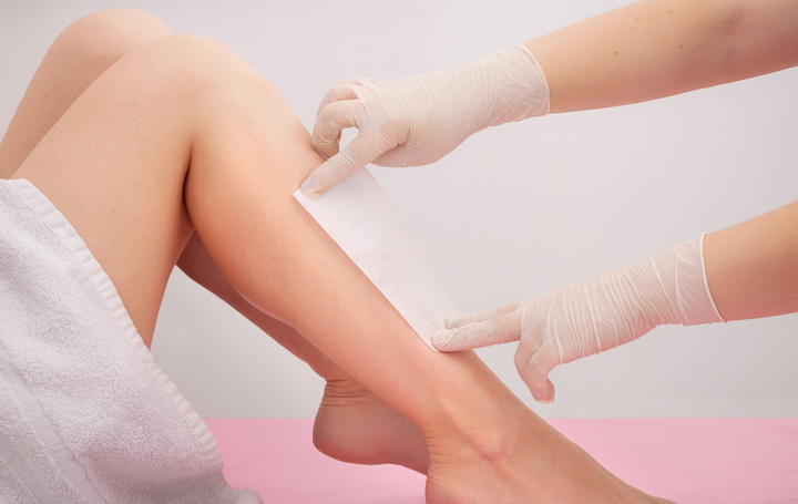 Gloved hands applying a leg wax treatment to a seated client’s lower leg
