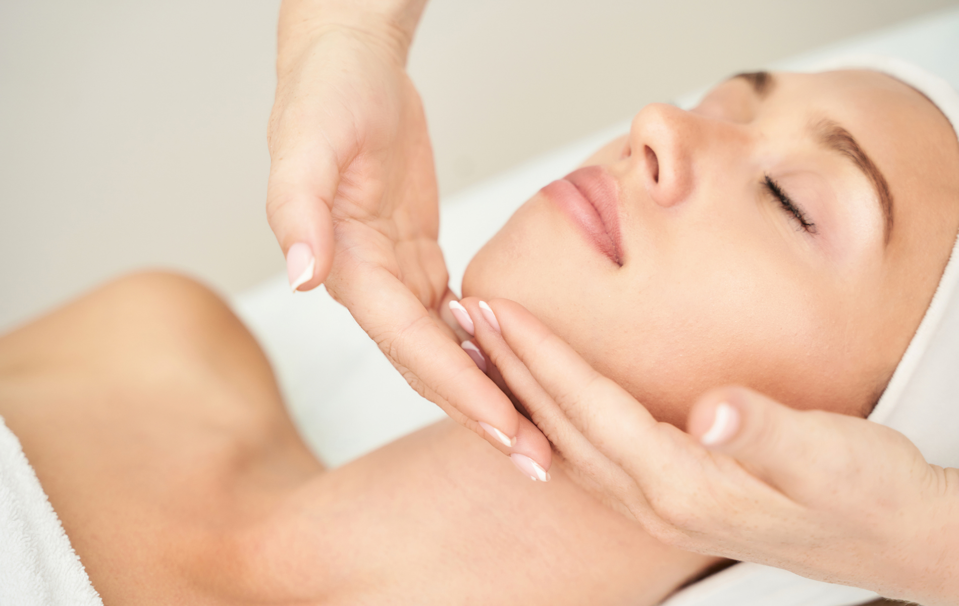 Hands giving a facial massage to a woman lying with eyes closed in a spa setting