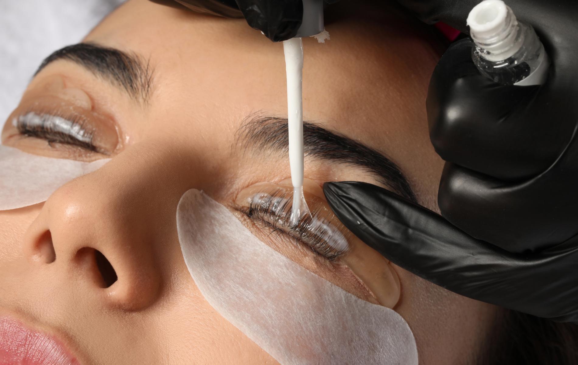 Lash technician applying treatment to closed eye with gel pads and black gloves
