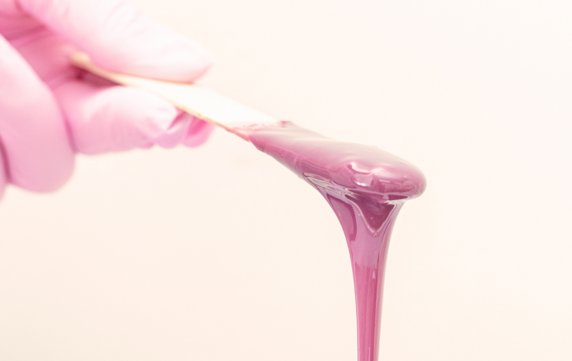 Hand in pink glove stretching purple wax or gel from a stick
