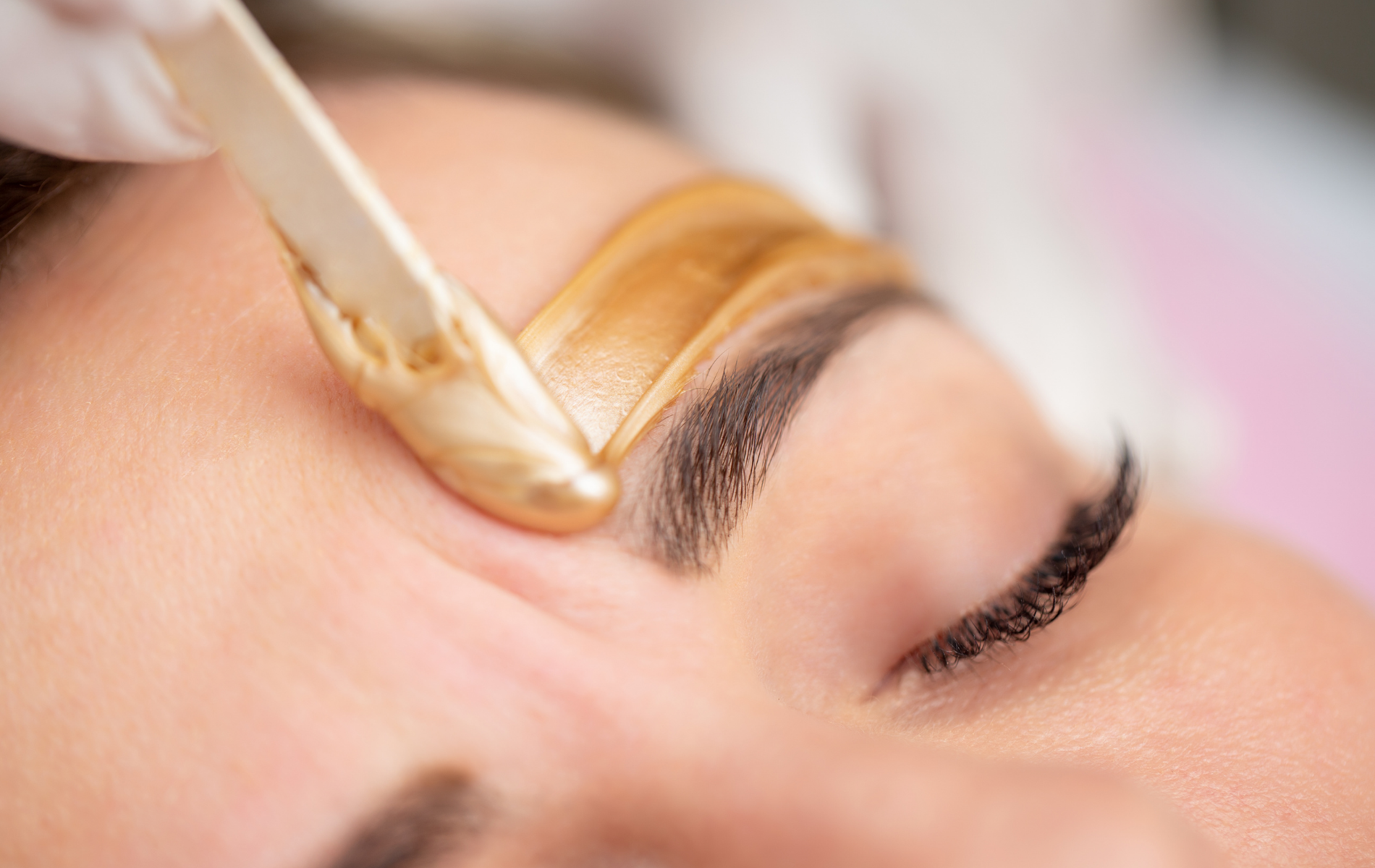 Wax applicator shaping an eyebrow during a cosmetic treatment