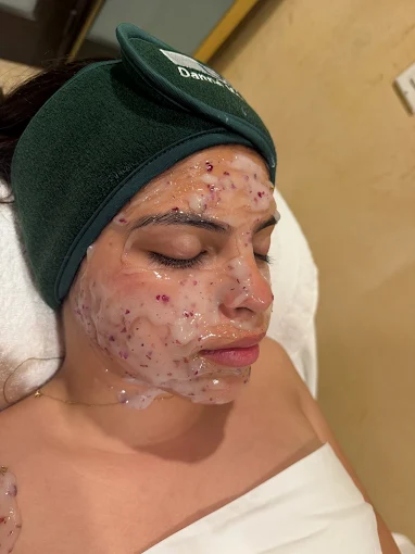 Person lying down with facial treatment mask and dark green head wrap, eyes closed on a white towel