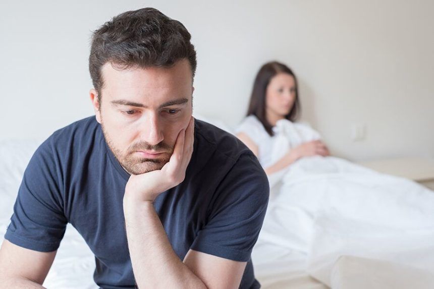 Woman embraces man, both smiling and looking at a smartphone. They are indoors.