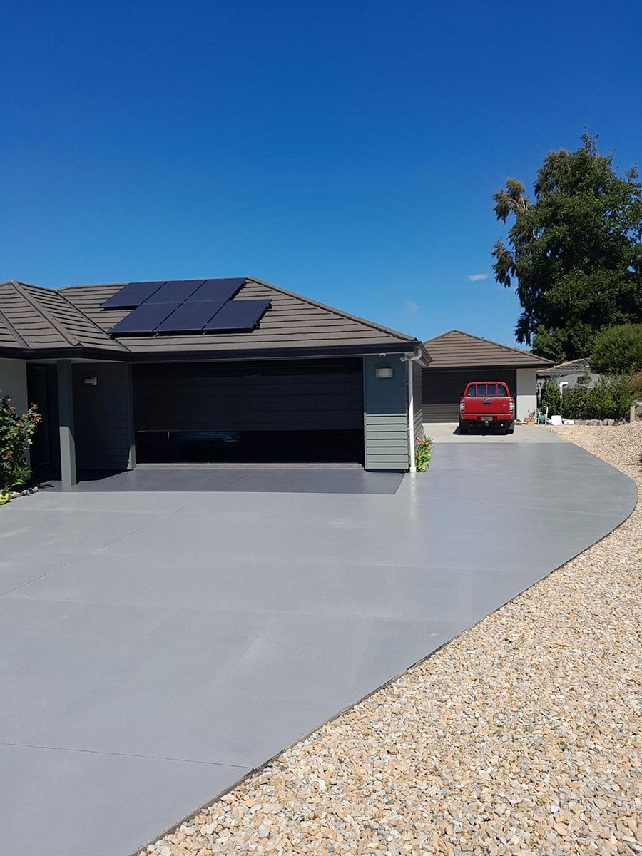 A house with a grey driveway, open garage door, red truck, and solar panels on the roof under a blue sky.