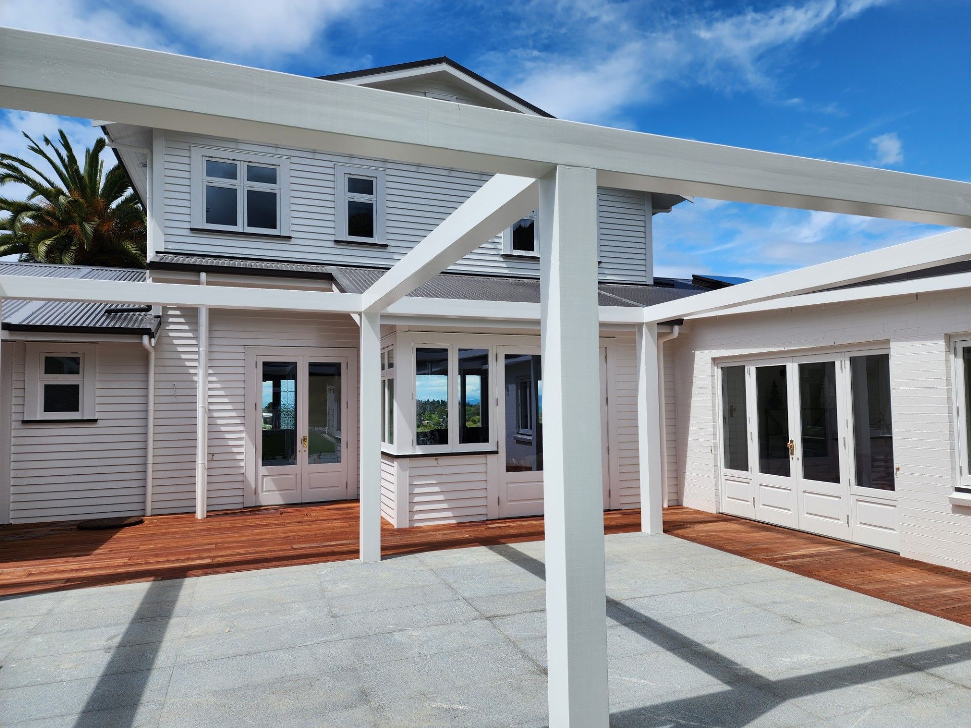 White house with pergola over a brick and stone patio on a sunny day.