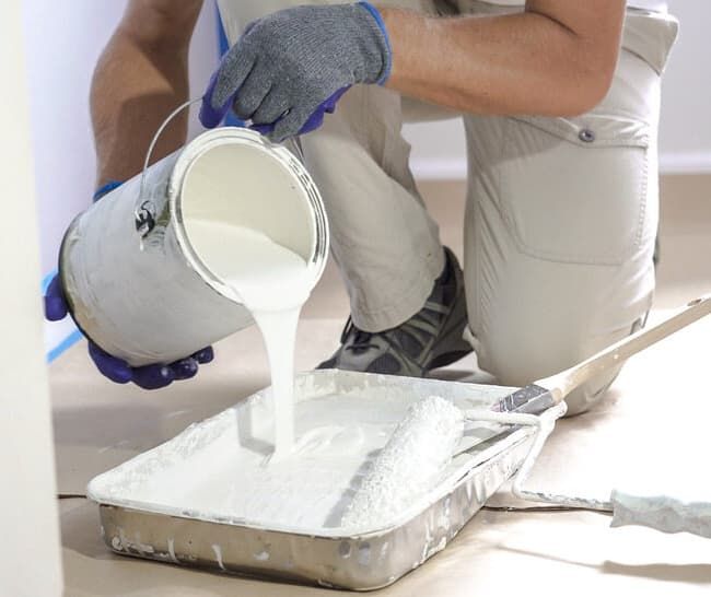 A Man Is Pouring White Paint Into A Paint Tray — Greg Cannon Painting In Maitland, NSW