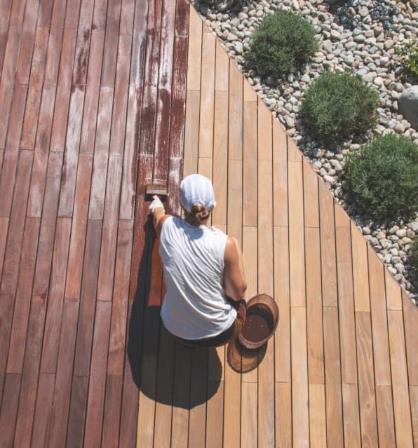 A Man Is Painting A Wooden Deck With A Brush — Greg Cannon Painting In Lake Macquarie, NSW