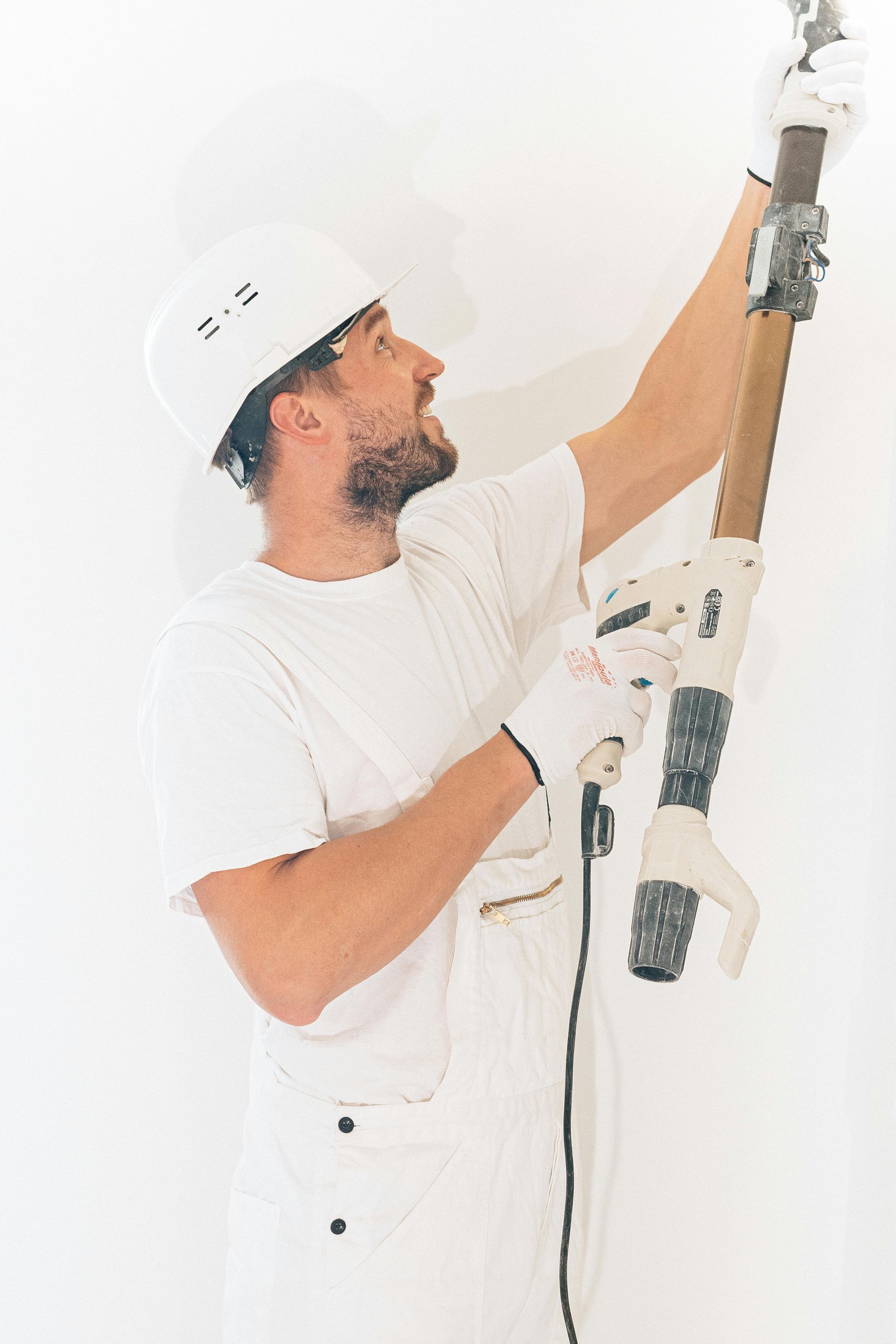 A Man Is Painting A Wall With A Painting Machine — Greg Cannon Painting In New Castle, NSW