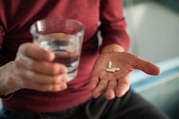 Hand holding several pills beside a glass of water.