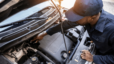 a mechanic wearing a hat doing an auto repair outside