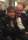 A man in a tuxedo sits next to a woman in a sequined jacket