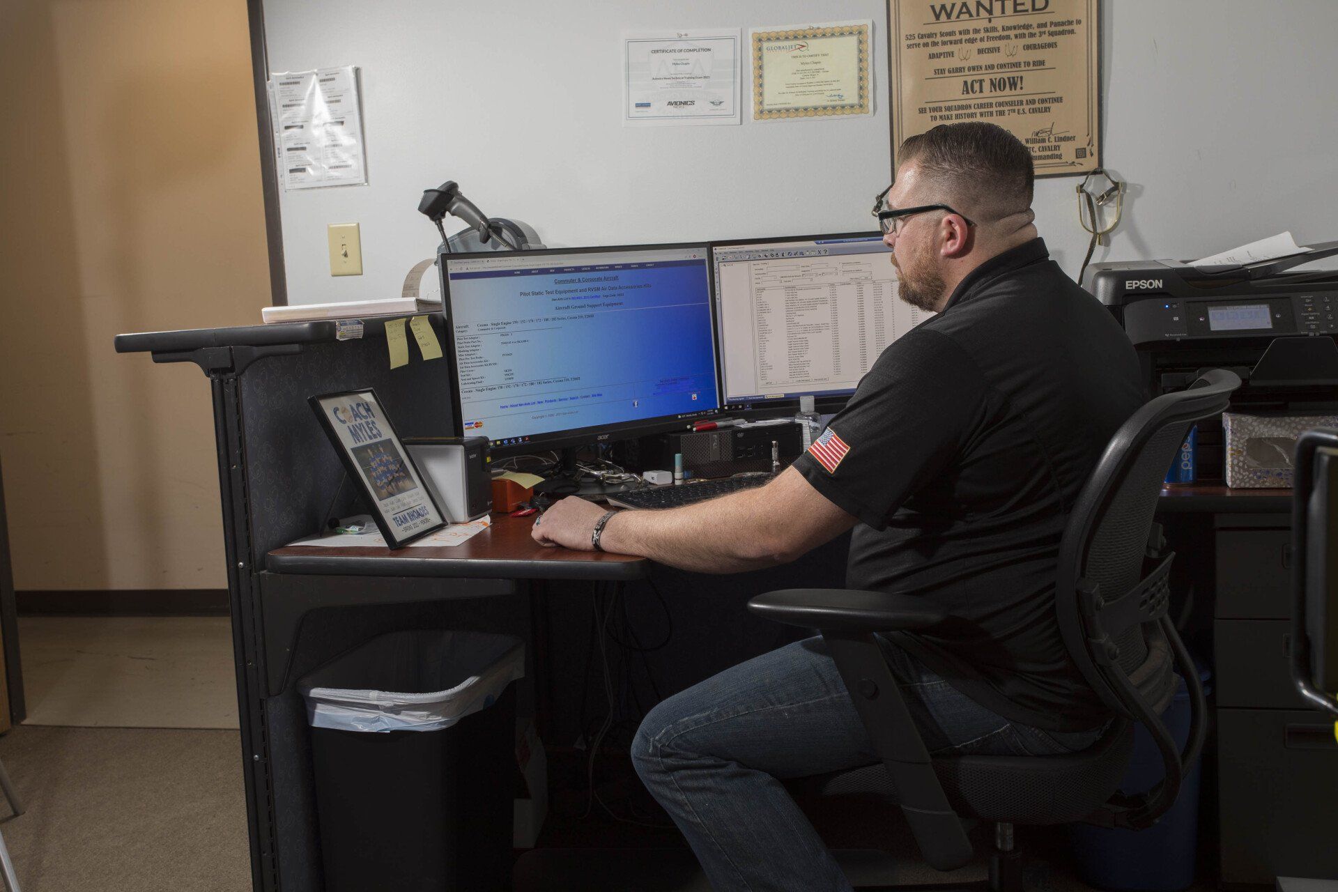 A man is sitting at a desk in front of two computer monitors.