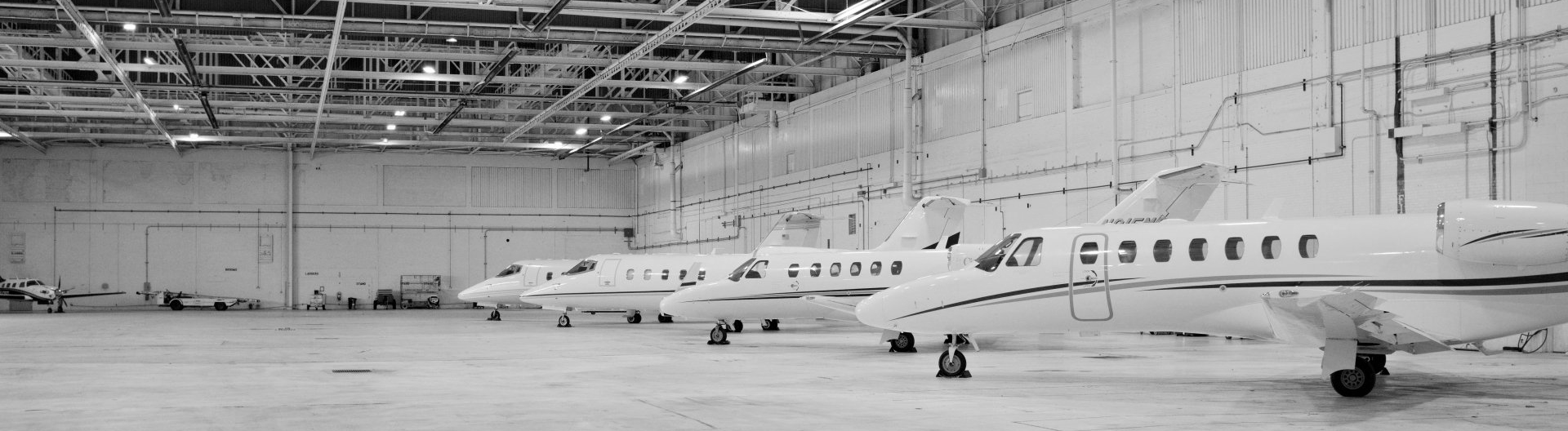 A row of private jets are parked in a hangar