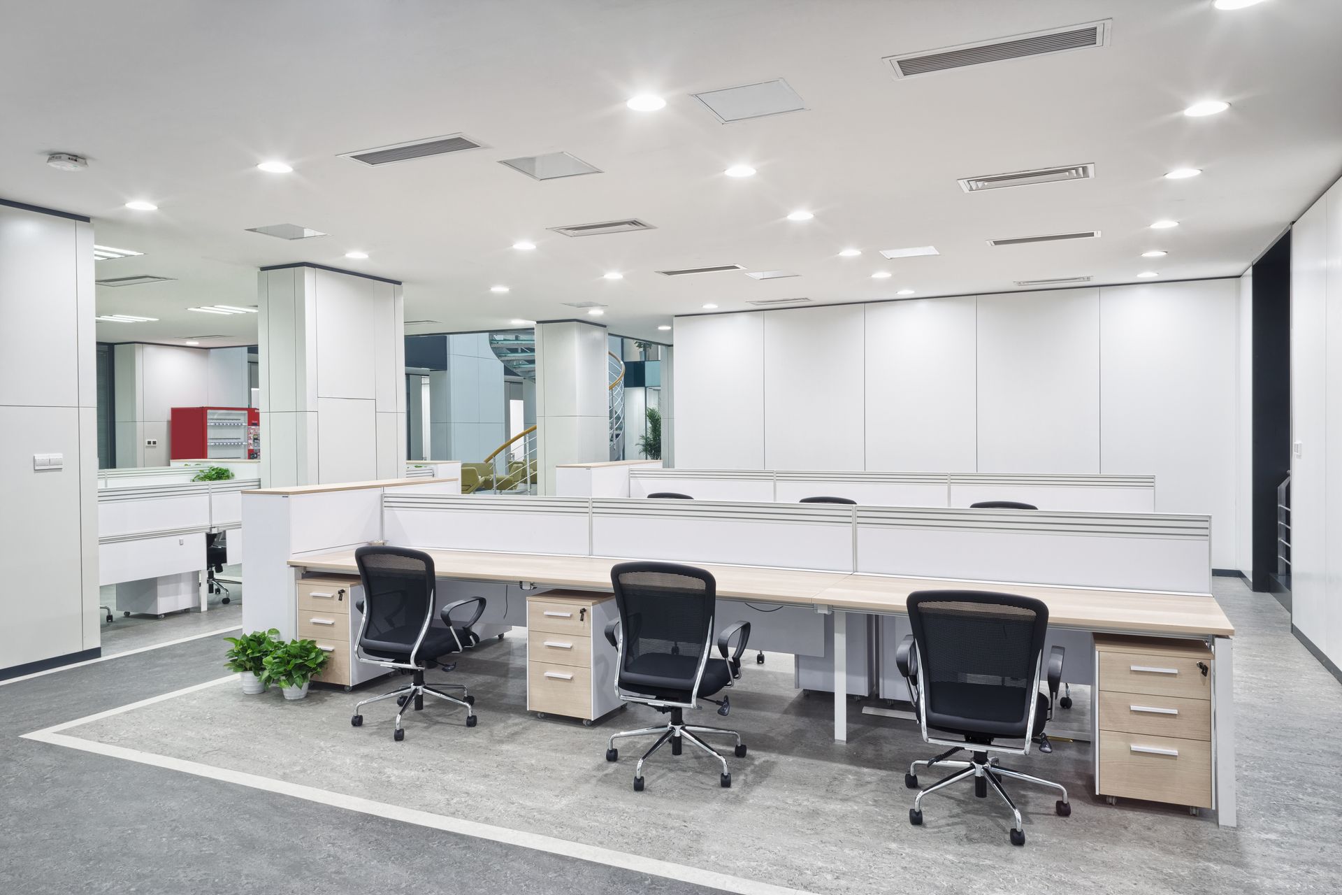 Modern, bright office space with desks, chairs, and overhead lighting. White walls, gray carpet.