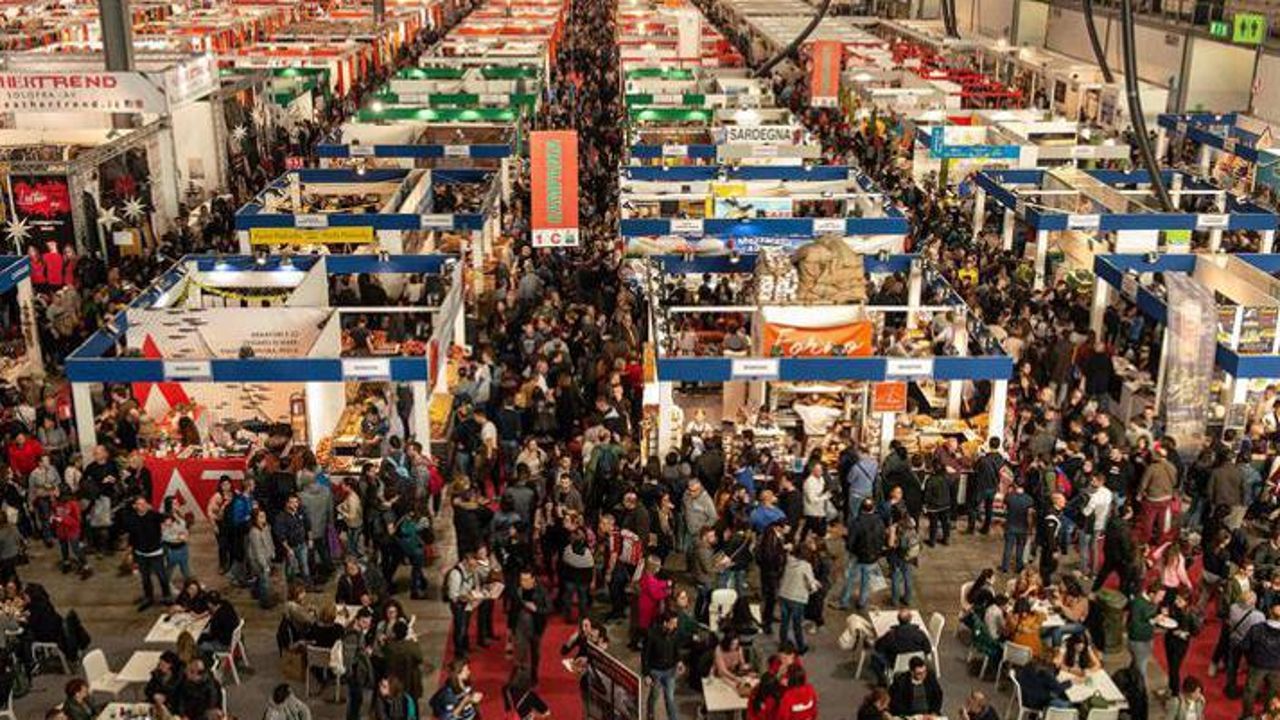 Crowded indoor trade fair with rows of booths and many people walking between aisles