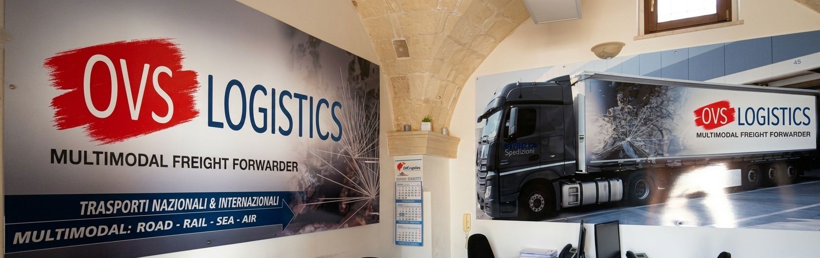Red and white OVS Logistics mural with a semi-truck in an indoor office or warehouse lobby
