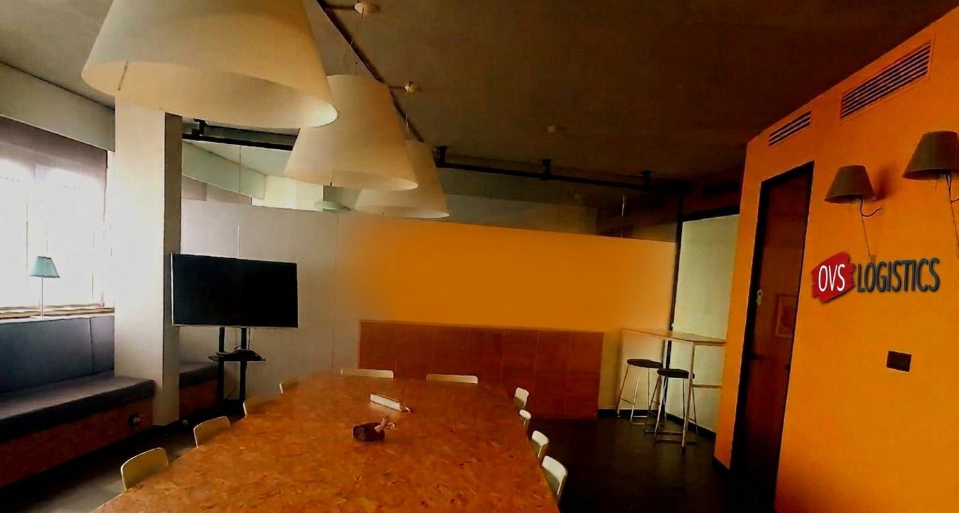 Modern meeting room with orange walls, long table, TV screen, and hanging lights