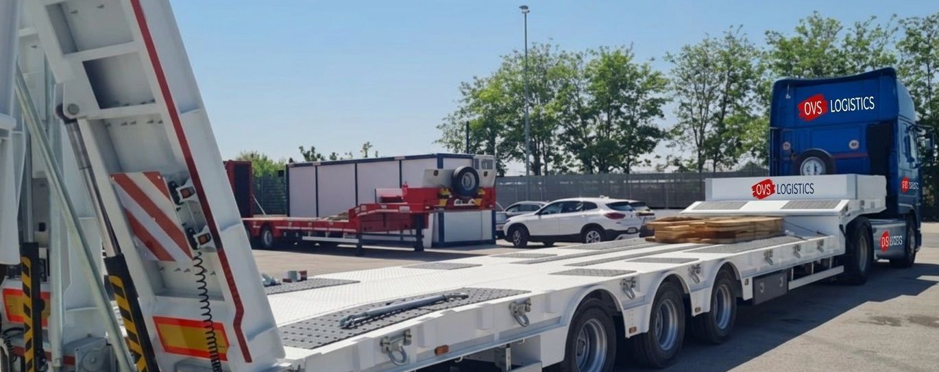 White flatbed tow truck hauling a red semi-trailer in a sunny parking lot