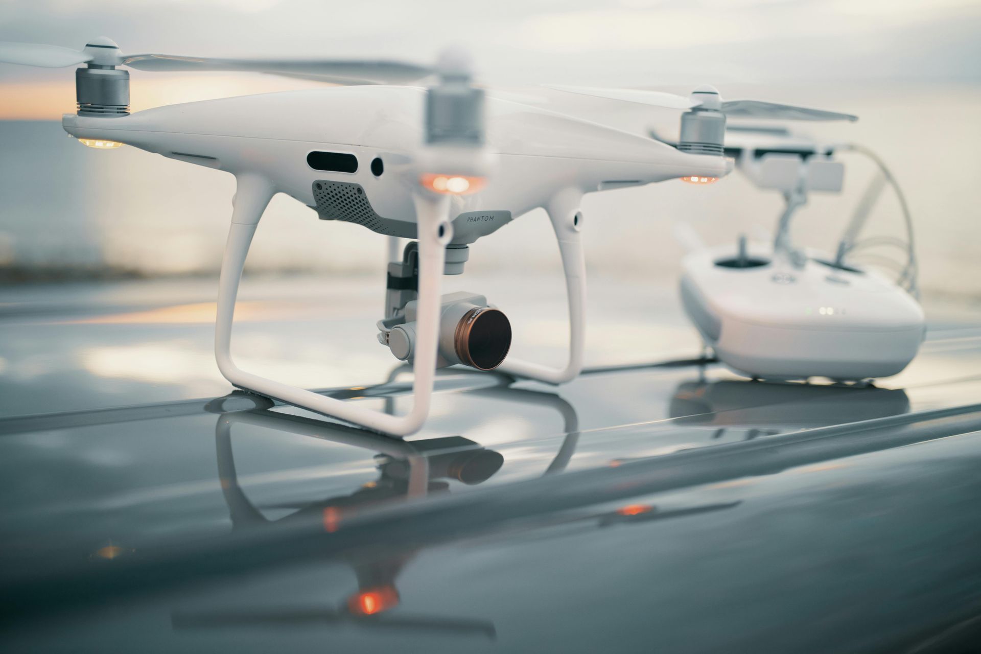 White drone on a reflective surface beside its remote controller, with propeller blades blurred in motion