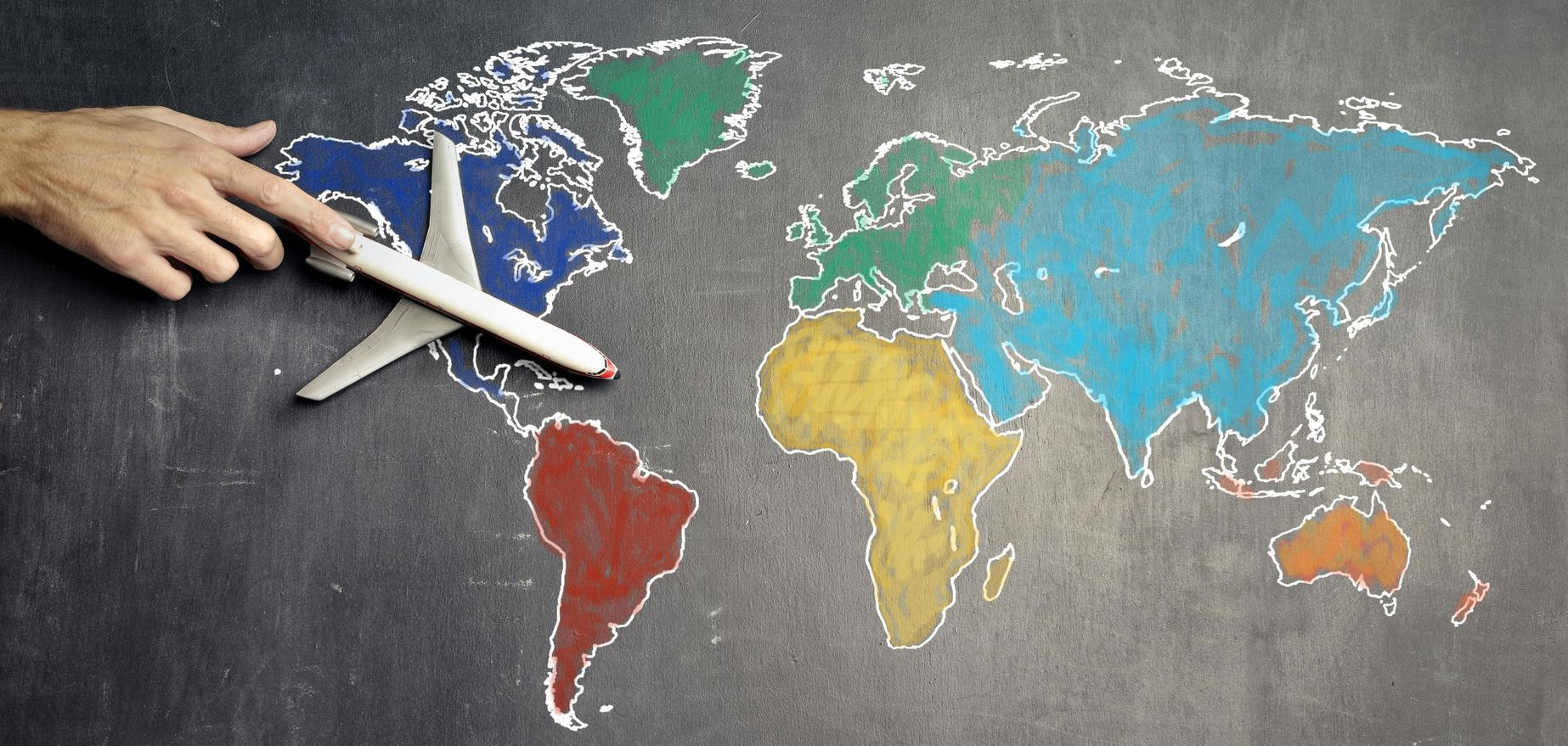 Hand placing an airplane over a colorful chalk world map on a blackboard