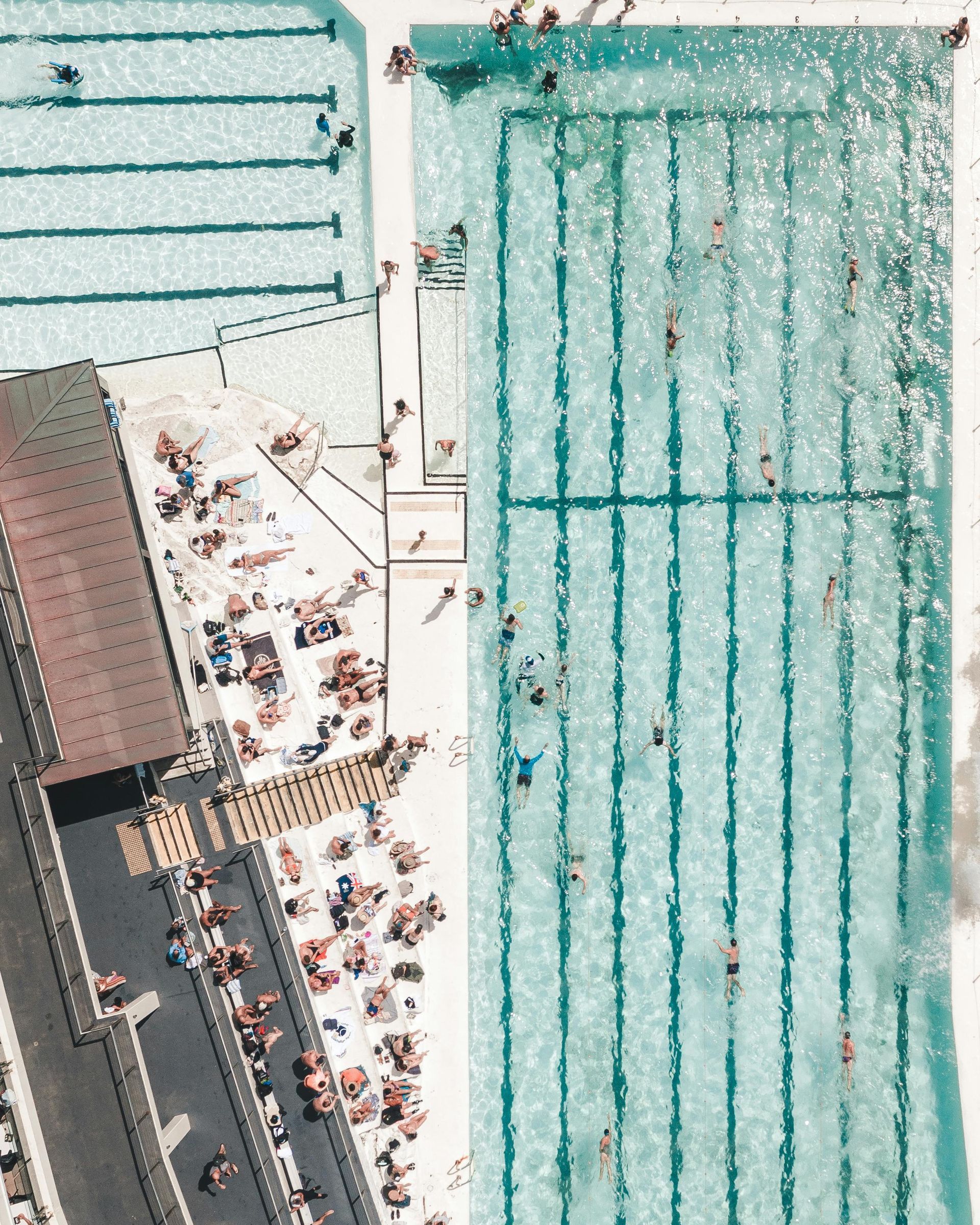 Aerial view of a crowded beach with turquoise swim lanes and people along the shore