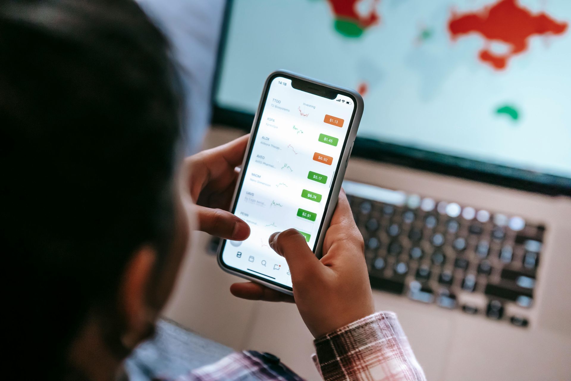 Person holding a smartphone with a chat app open, in front of a laptop displaying a world map