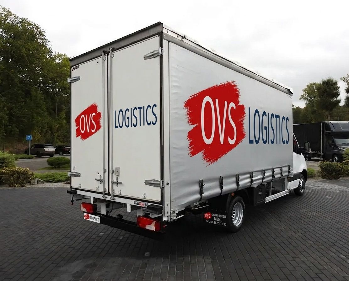 White OVS Logistics box truck parked on a paved lot, rear and side visible.