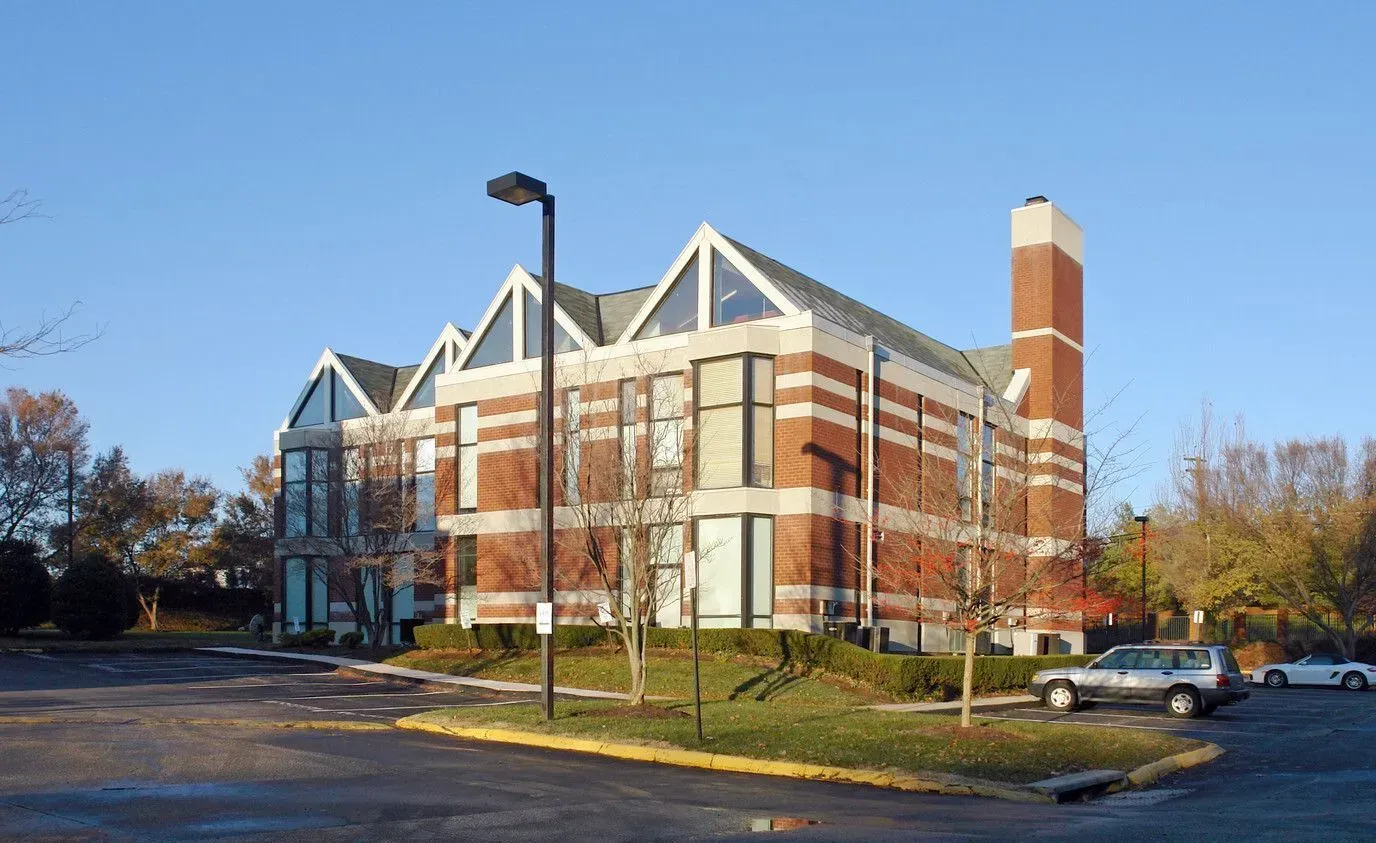 Brick academic building with white roof trusses and a tall chimney under a blue sky