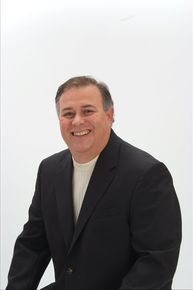 Smiling man in a dark suit and white shirt against a plain white background