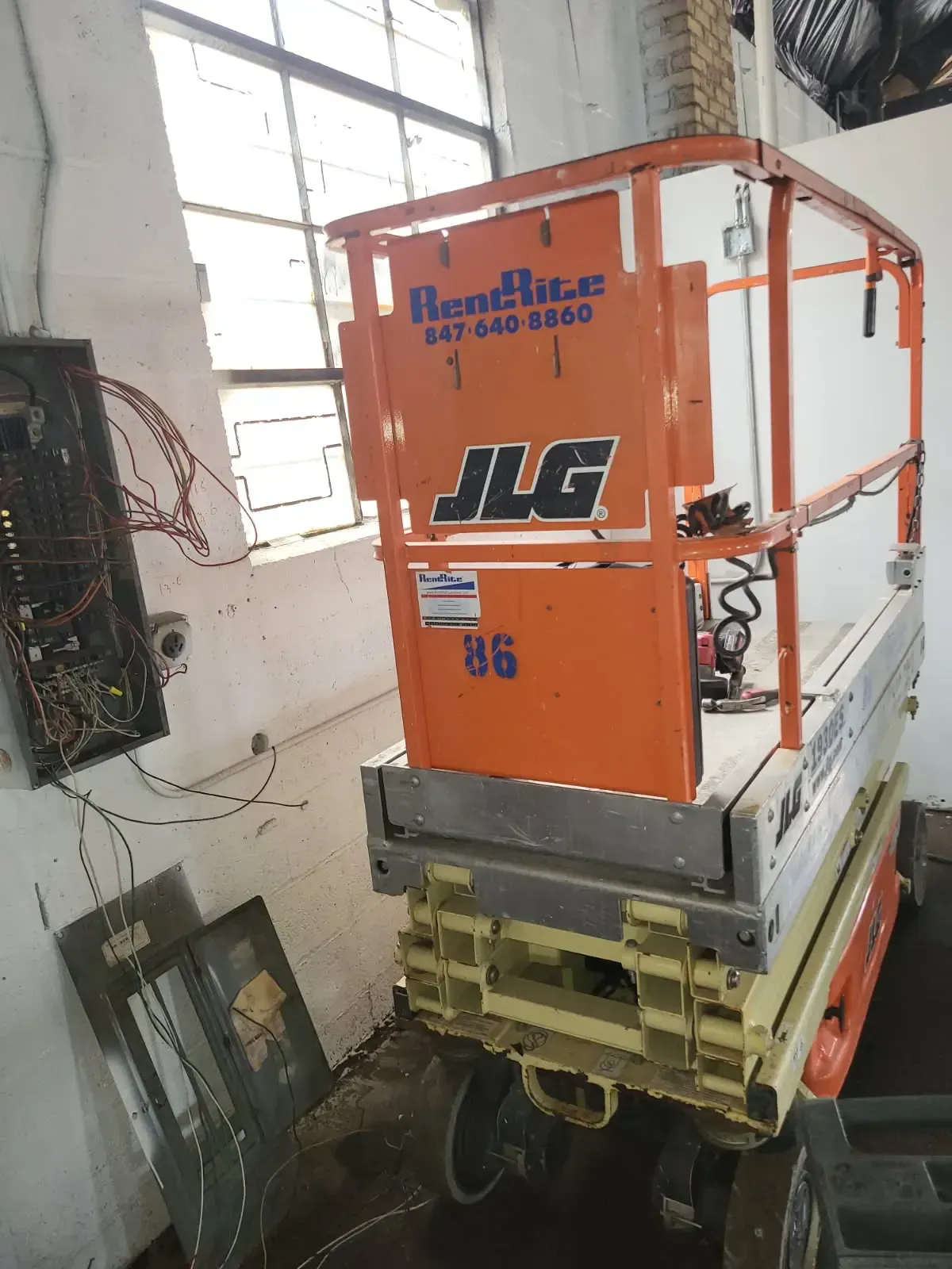 A scissor lift platform positioned indoors with electrical wiring and control panels visible nearby during an installation