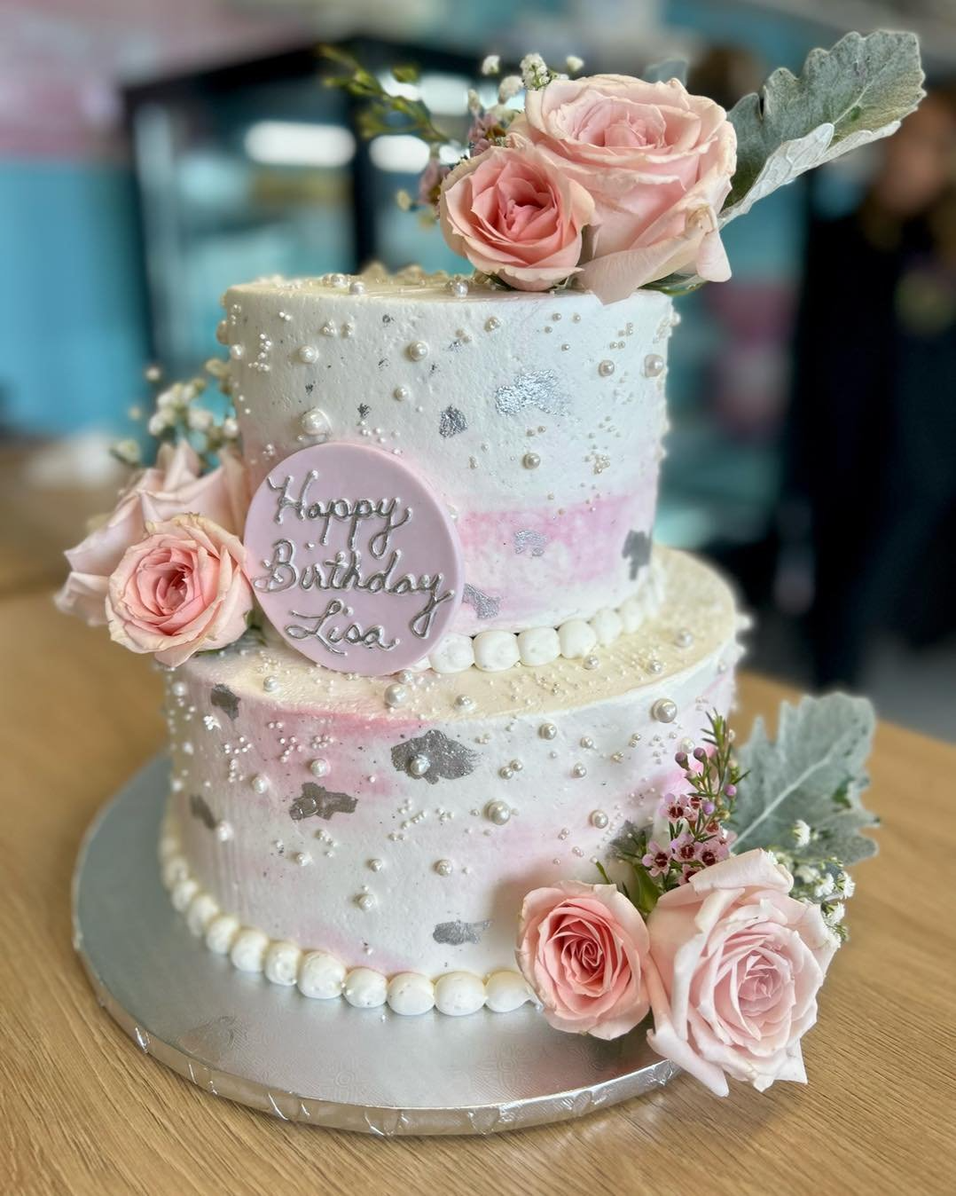 A birthday cake with pink roses and pearls on a wooden table.