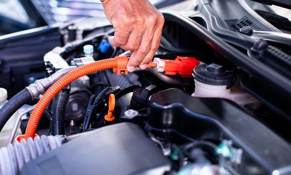 Person using orange jumper cables to connect a car battery in an engine bay