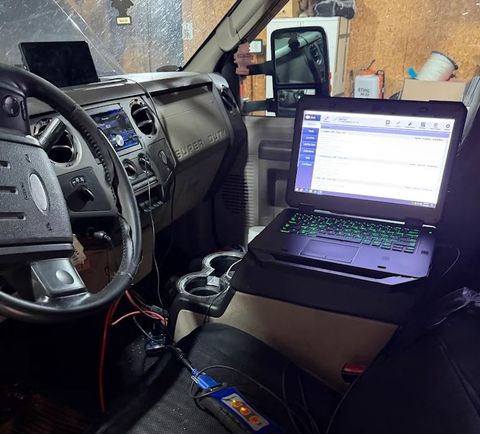 Car interior with open laptop on passenger seat and dashboard visible, suggesting a mobile workstation.