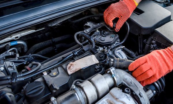 Gloved hands inspecting a car engine under the hood in a garage