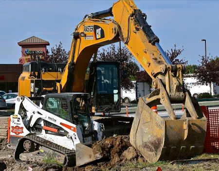 Excavator and skid steer working on dirt at a construction site on a sunny day