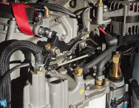 Close-up of a mechanical engine assembly with hoses, bolts, and red strap in a workshop setting