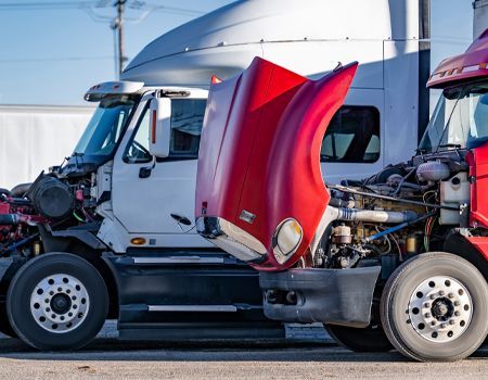 White semi-truck with a red hood and exposed engine parked on a road