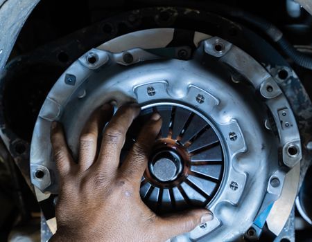 Hand inspecting a car clutch assembly with visible pressure plate and spring fingers