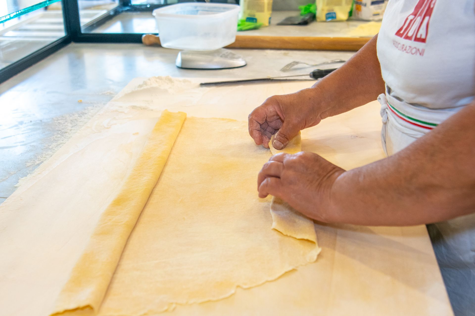 Mani che stendono una sottile sfoglia di pasta su un piano di lavoro infarinato in cucina
