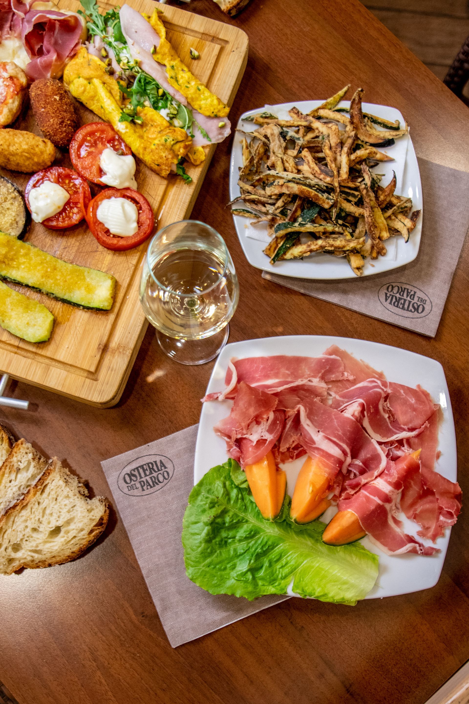Assortimento di tapas con vino su un tavolo di legno, tra cui prosciutto crudo, patatine fritte e pane.