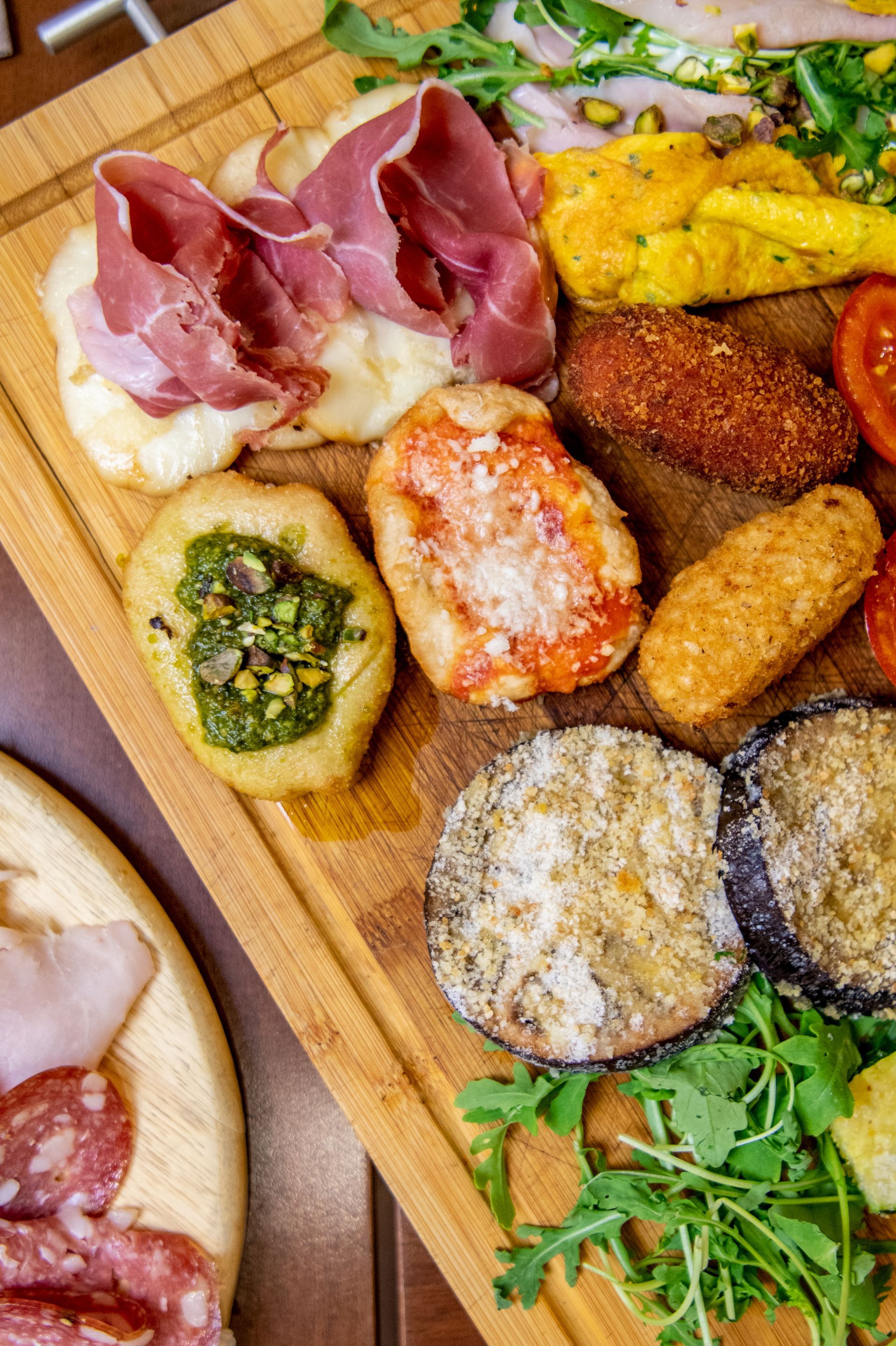 Assortimento di antipasti su un tagliere di legno con salumi, peperoni ripieni ed erbe aromatiche.