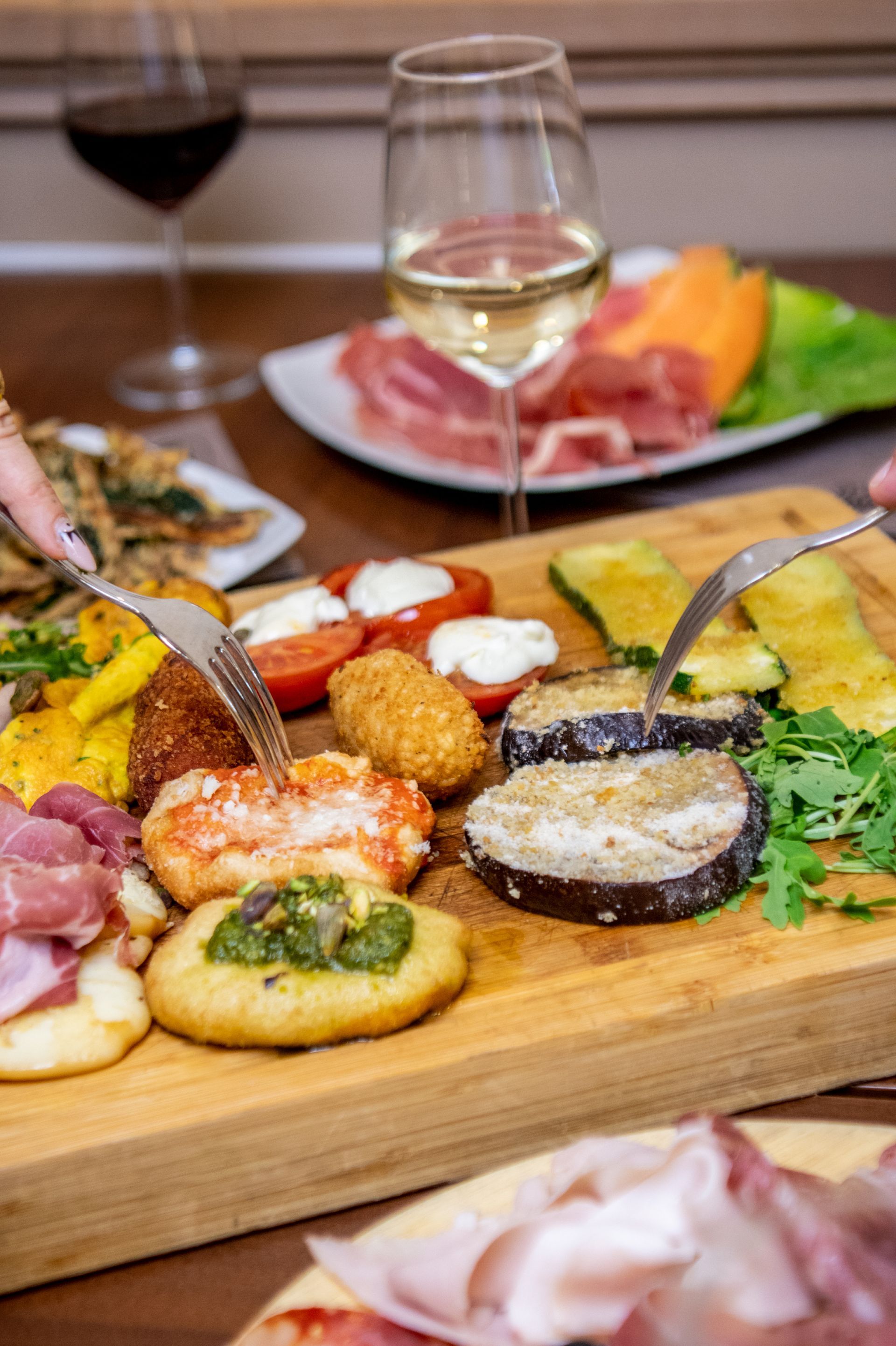 Assortimento di tapas su un tagliere di legno con bicchieri da vino e salumi su un tavolo.