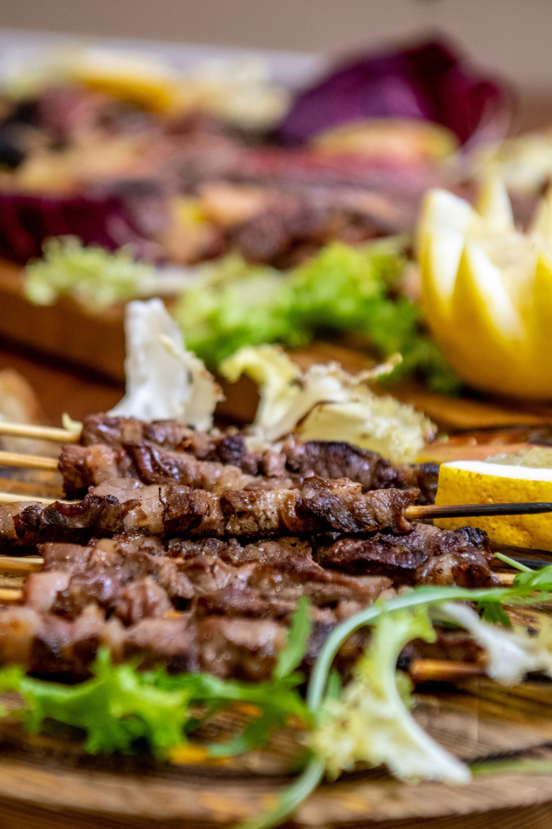 Spiedini di carne grigliata su un piatto di legno con lattuga, spicchi di limone e pane piatto.