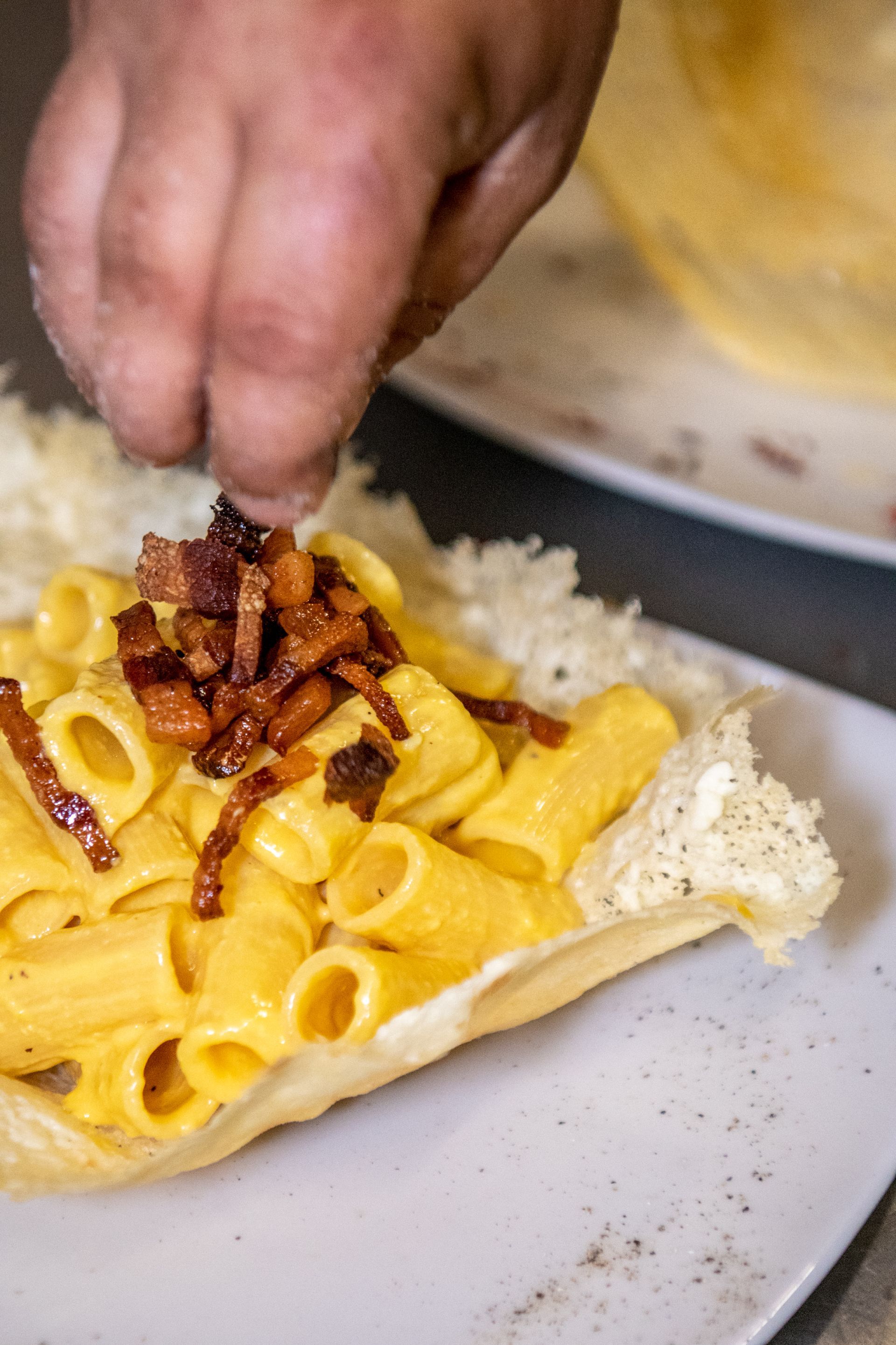 Maccheroni al formaggio cremosi conditi a mano e pancetta croccante su un piatto