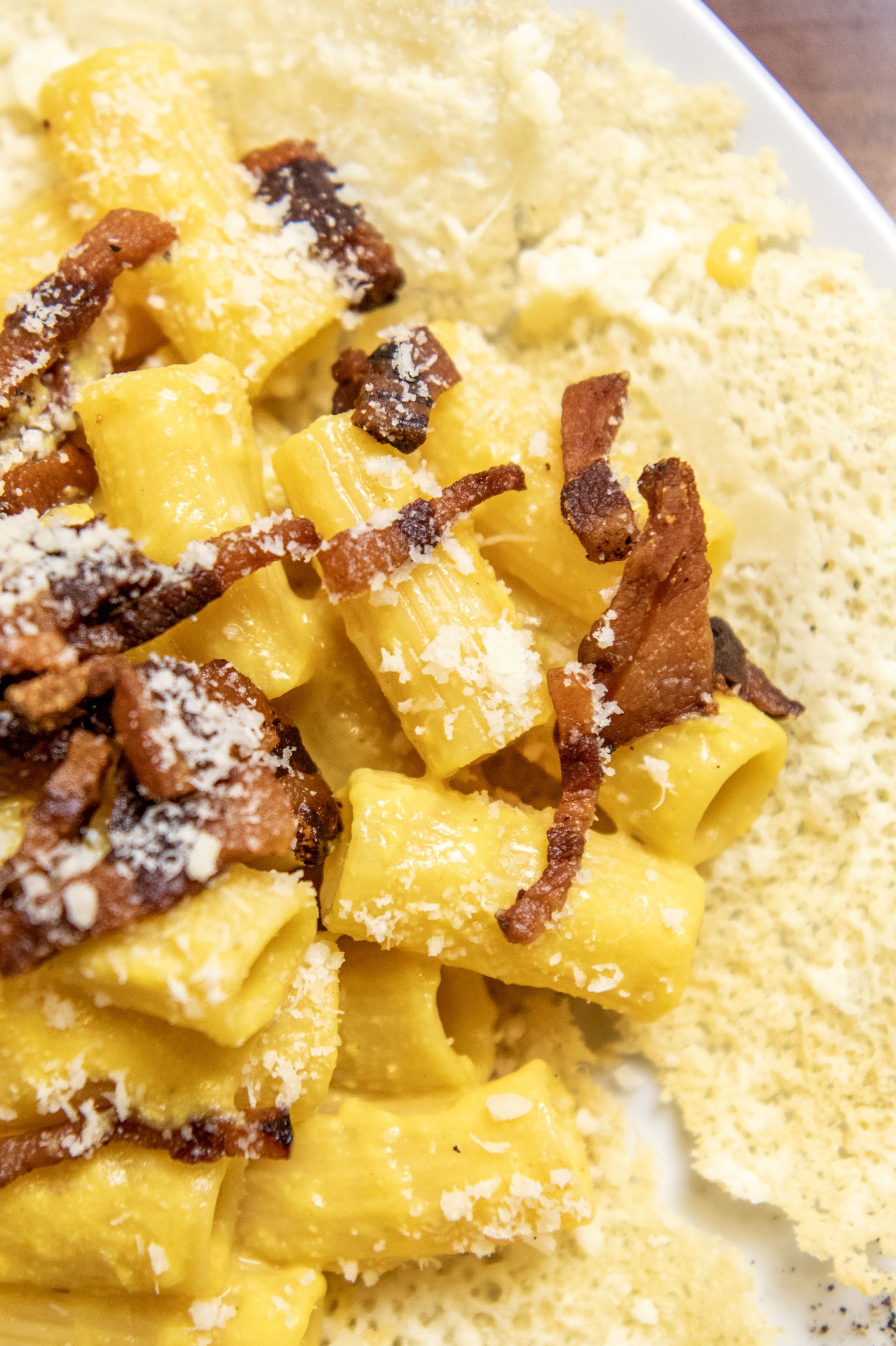Pasta con salsa gialla alla panna, pancetta croccante e formaggio grattugiato su un piatto bianco