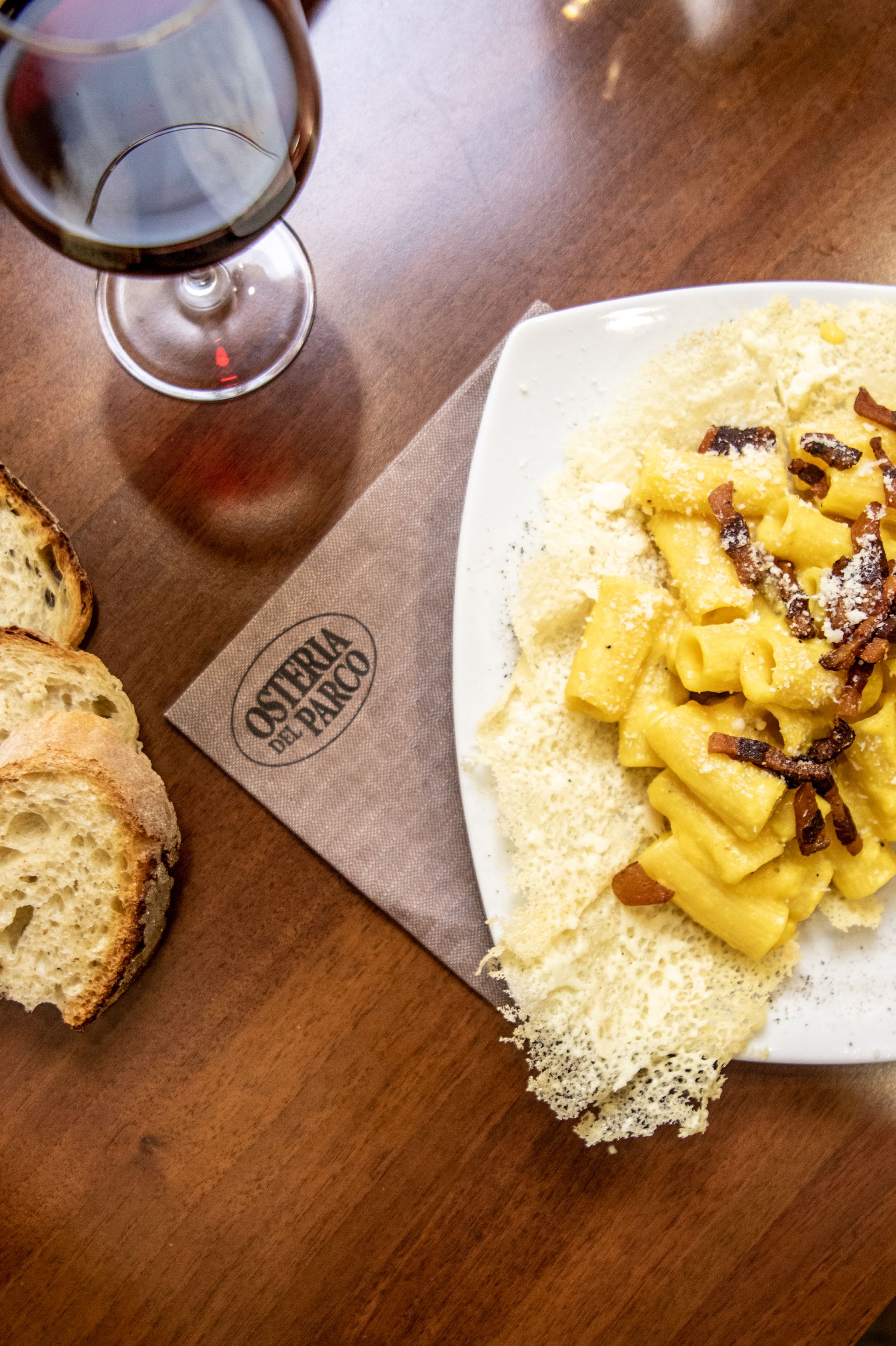 Vino, pane e un piatto bianco di gnocchi alle erbe su un tavolo di legno con un tovagliolo sotto il piatto