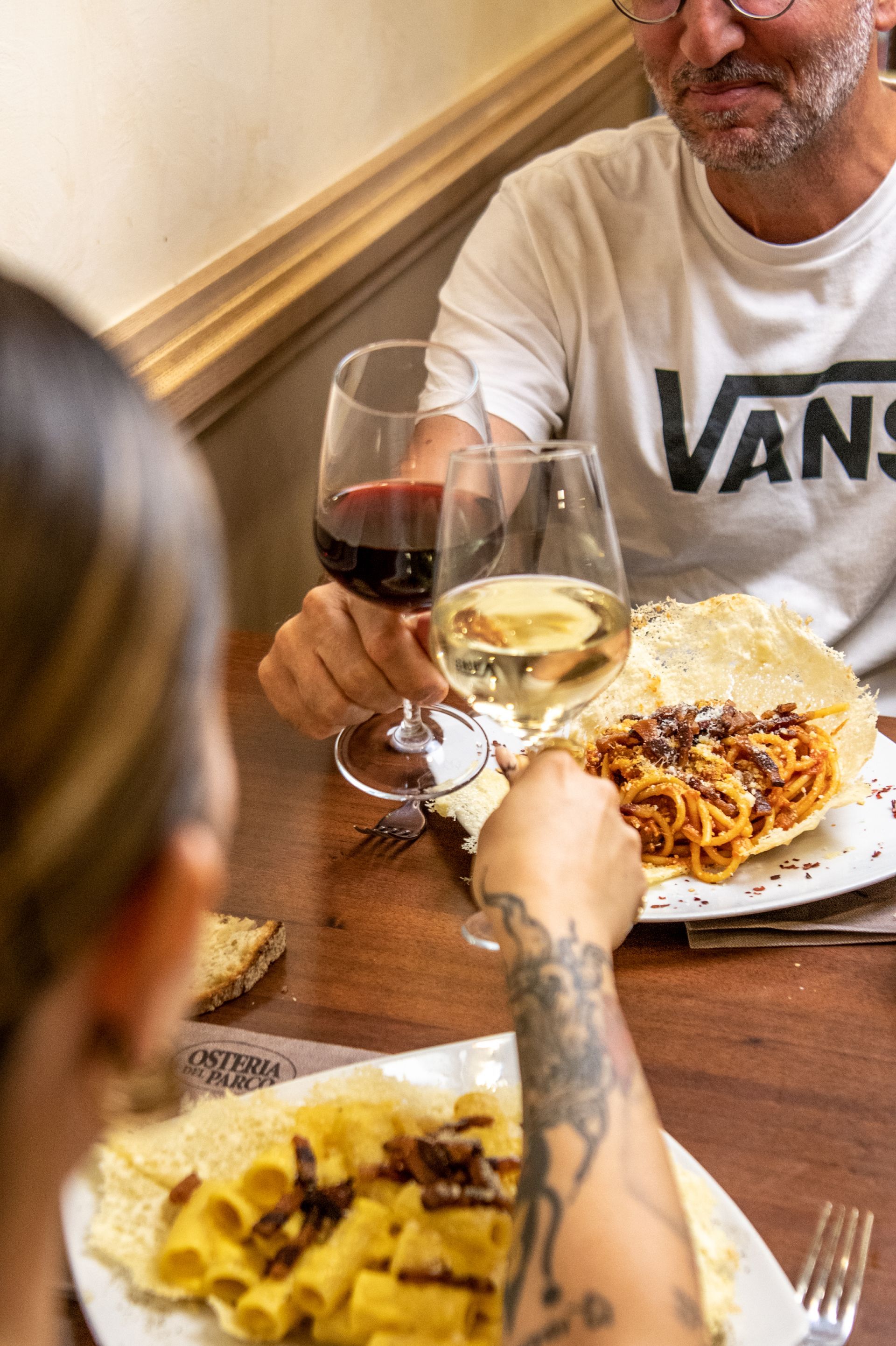 Persone che brindano attorno a un tavolo di legno con pasta, vino e piatti in un'atmosfera accogliente da ristorante.